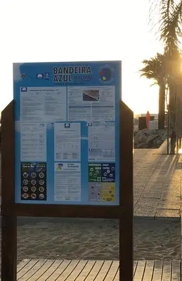 a sign on the beach with the sun in the background at Apartamento Quarteira T1 in Quarteira