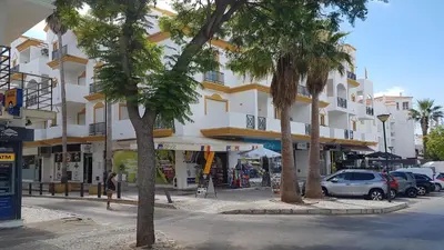 a building with palm trees in front of a street at Apartment on The Strip Albufeira in Albufeira