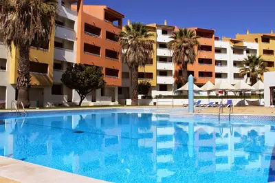 a swimming pool in front of a building with palm trees at Apartamento Bela Vista in Albufeira