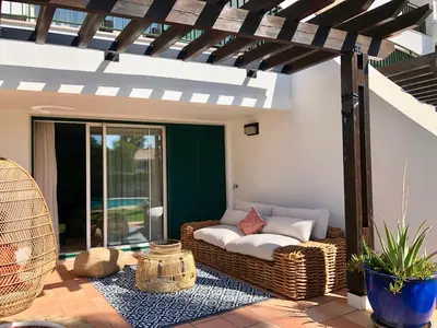 a patio with a wicker couch under a pergola at Birdsong Vila Sol Village in Vilamoura