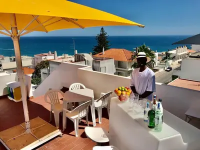 a woman standing on a balcony with a table and an umbrella at Hotel da Gale in Albufeira
