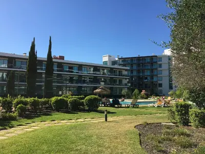 a park with a building in the background with people sitting on benches at Golf Residence Apartment in Vilamoura