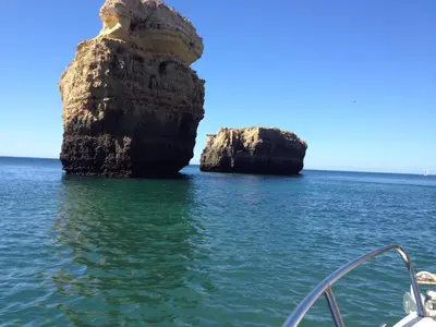 a rock formation in the water next to a boat at Vista das Ondas Olhos de Agua in Albufeira