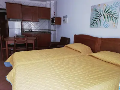 a bedroom with a bed and a kitchen with a table at Apartamentos Arcada in Quarteira