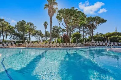 a swimming pool with chairs and palm trees at Four Seasons Country Club in Quinta do Lago