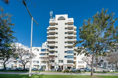 a tall white building with cars parked in a parking lot at Apartamento Mar in Quarteira