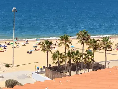 a beach with palm trees and people on the sand at Regueiró Quarteira Beach Apartment in Quarteira