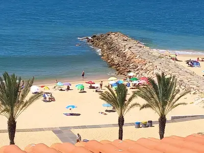 a group of people on a beach with umbrellas at Regueiró Quarteira Beach Apartment in Quarteira