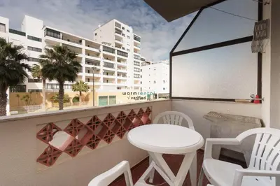 a balcony with a white table and chairs and a building at Regueiró Quarteira Beach Apartment in Quarteira