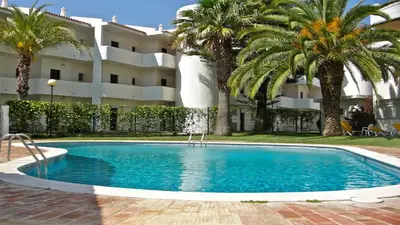 a swimming pool in front of a building with palm trees at Terraços do Mar 46- Clever Details in Vilamoura