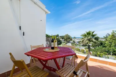 a red table with two chairs and wine bottles on a balcony at BmyGuest - Quinta do Lago Terrace Apartment II in Quinta do Lago