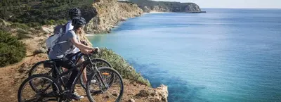 a man riding a bike on a cliff overlooking the ocean at VilamouraSun Aquamar 110 - Pool and Marina View in Vilamoura