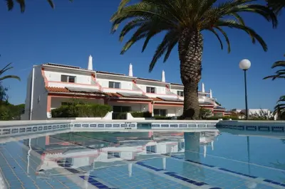 a swimming pool with a palm tree and a building at Moradias Villas Joinal in Albufeira