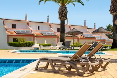 a resort with a pool and chairs and palm trees at Moradias Villas Joinal in Albufeira
