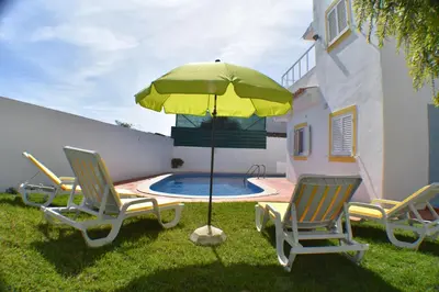 a group of chairs and an umbrella next to a pool at Villa Amendoeira-POOL HEATED - By Algarkasa in Guia