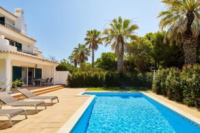 a swimming pool with chairs and a house at Ancão Gardens in Quinta do Lago