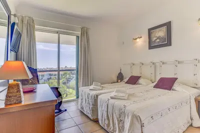 a bedroom with two beds and a desk and a window at Apartamento Vila Sol com terraço e jacuzzi privad in Quarteira