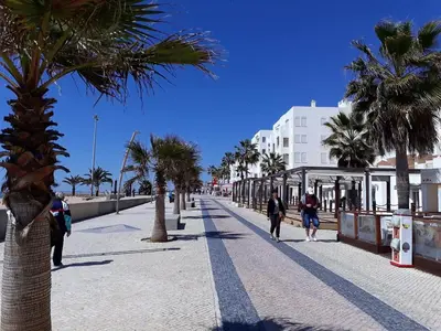 a street with palm trees and people walking down it at Mamamia AC&Vista Magnifica in Quarteira