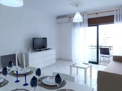 a white living room with a table and a tv at SATÉLITE AC&Garagem in Quarteira