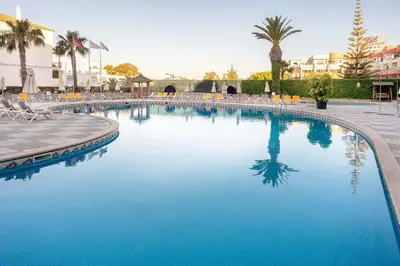 a large blue swimming pool with chairs and palm trees at Muthu Oura Praia Hotel in Albufeira