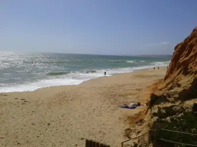 a beach with people walking on the sand and the ocean at Apartamento Praia da Falésia in Albufeira