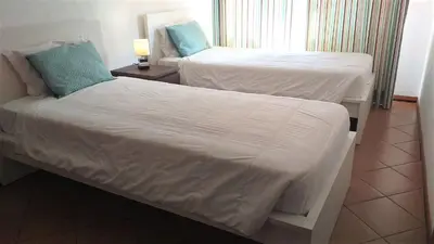 a bedroom with two beds with white sheets and blue pillows at T2 Mira Praia 4- Familiar, 80mt Praia, Wifi in Quarteira