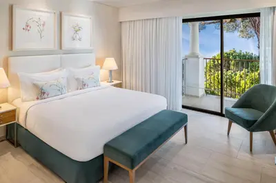 a bedroom with a bed and a chair and a window at Pine Cliffs Gardens in Albufeira