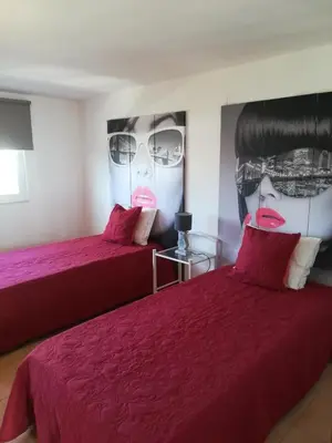 a bedroom with two beds with red sheets and a large painting of two faces at Quinta Das Palmeiras in Quarteira