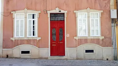 a red door on the side of a building with two windows at Hostel A Casa da Árvore in Faro