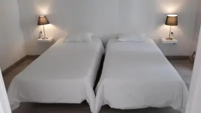 two beds in a room with white sheets and lamps at Hostel A Casa da Árvore in Faro