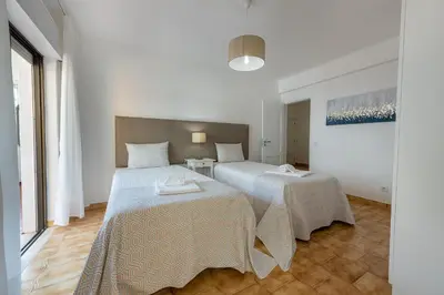 two beds in a room with white walls and wood floors at Carol & Vany in Quarteira