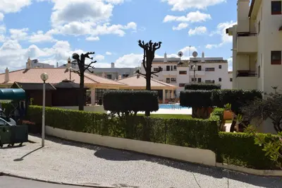 a hedge in front of a building with a pool at Apartamento T2 com Piscina e Wifi a 350 metros da Praia in Roja- Pé