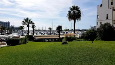 a park with palm trees and a parking lot with cars at Marina Apartment in Quarteira