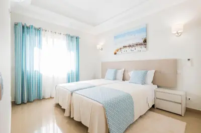 two beds in a white room with blue curtains at Lakeside Country Club - Apartamentos Turísticos in Quinta do Lago