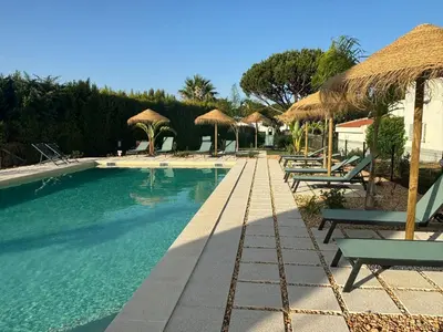 a swimming pool with chairs and straw umbrellas at Vale do Lobo - Casa de La Rosa in Vale do Lobo