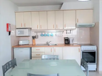 a kitchen with white cabinets and a table with chairs at Sol europa- Vista Mar, 150mt Praia, Wifi in Quarteira