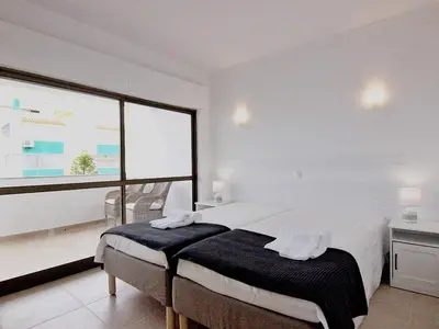 a white bedroom with a bed and a large window at Amendoeiras I - Central Vilamoura in Vilamoura