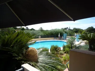 a swimming pool with palm trees and a black umbrella at Corcovada 37 in Albufeira
