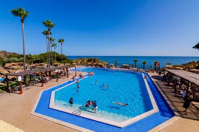 a large swimming pool with people in it next to the ocean at Auramar Beach Resort in Albufeira