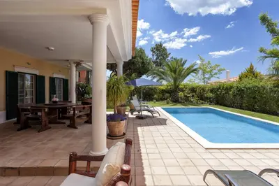 a patio with a pool and a table and a house at Martinhal Quinta Family Resort in Quinta do Lago