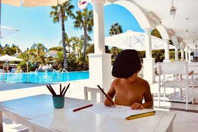 a little boy sitting at a table writing on a paper at Martinhal Quinta Family Resort in Quinta do Lago