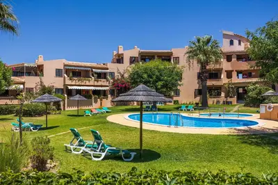 a resort with a pool and some chairs and an umbrella at Clube Maria Luisa in Albufeira