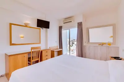 a bedroom with a white bed and a desk and a window at Vila Recife Hotel in Albufeira