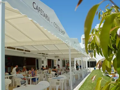 a group of people sitting at tables under a white umbrella at Hotel Apartamento Brisa Sol in Albufeira