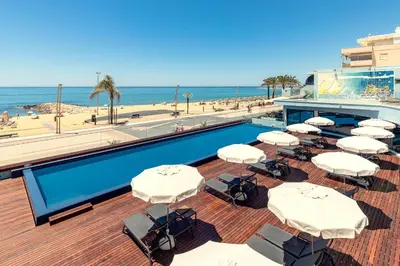 a swimming pool with white umbrellas and the beach at Dom Jose Beach Hotel (Plus) in Quarteira