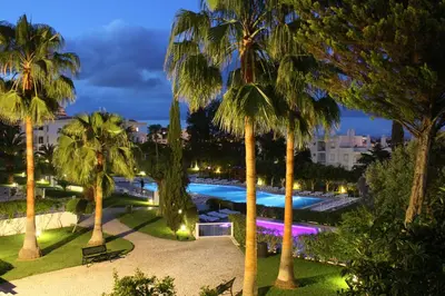 a view of a pool with palm trees at night at Vila Petra in Albufeira