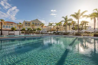 a large swimming pool with palm trees and buildings at Domes Lake Algarve, Autograph Collection in Vilamoura