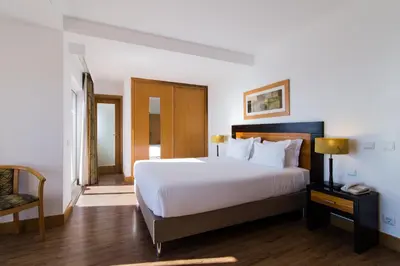a bedroom with a large white bed and a chair at Hotel Quarteirasol in Quarteira