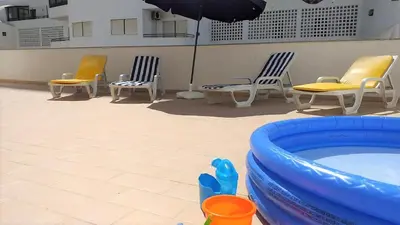 a group of chairs and a pool with an umbrella at T2 Tahíti - Terraço, Familiar, Garagem, Wifi in Quarteira