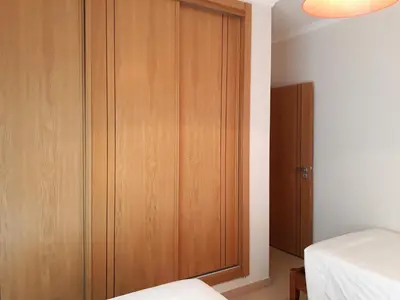 a bedroom with a wooden cabinet next to a bed at T2 Tahíti - Terraço, Familiar, Garagem, Wifi in Quarteira